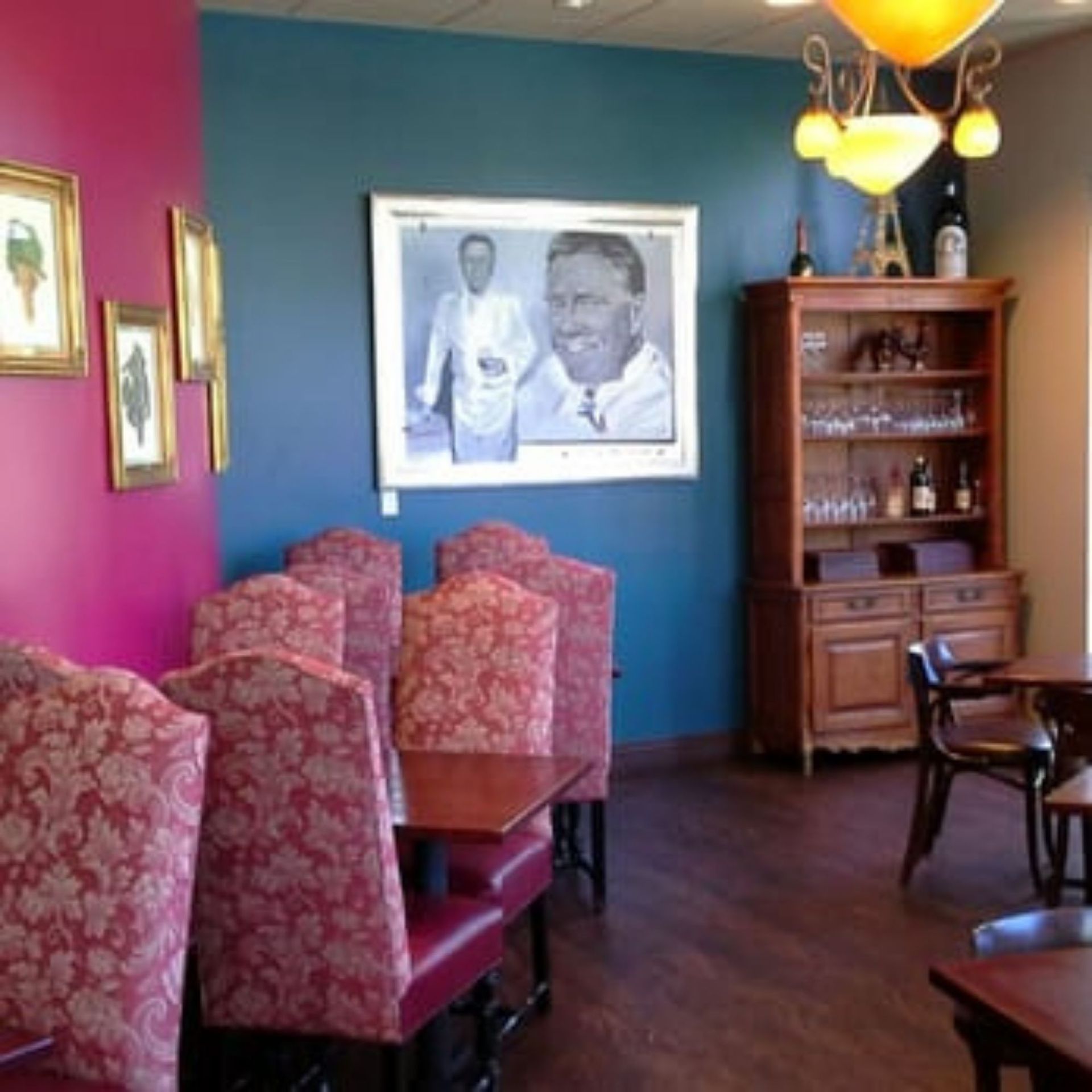 The right color - Restaurant interior with burgundy chairs, a wooden cabinet, and portraits on colorful walls.