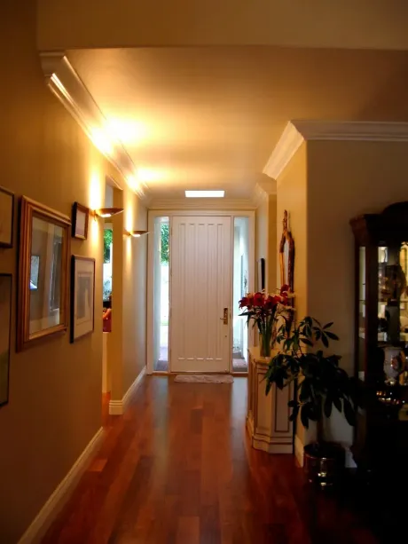 The right color - Long hallway with hardwood floor, leading to a white door. Tan walls with artwork, built-in lighting.