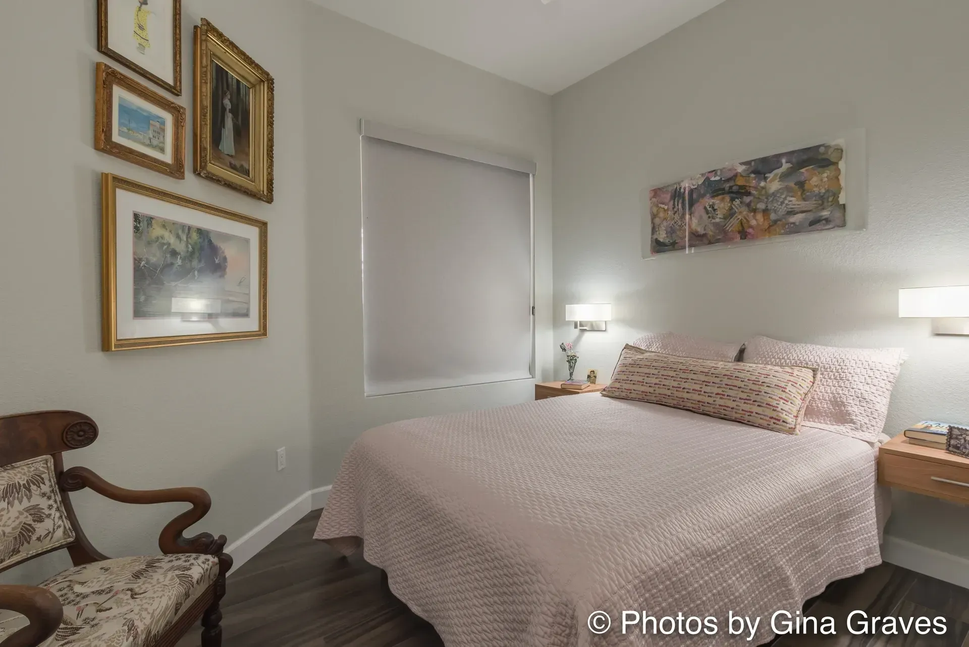The right color - Bedroom with a bed, artwork, a chair, and a small bedside table. Light pink bedding, light gray walls.