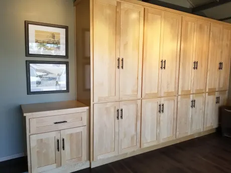 The right color - Light wood cabinets with black handles, next to a small cabinet and framed pictures, in a room.