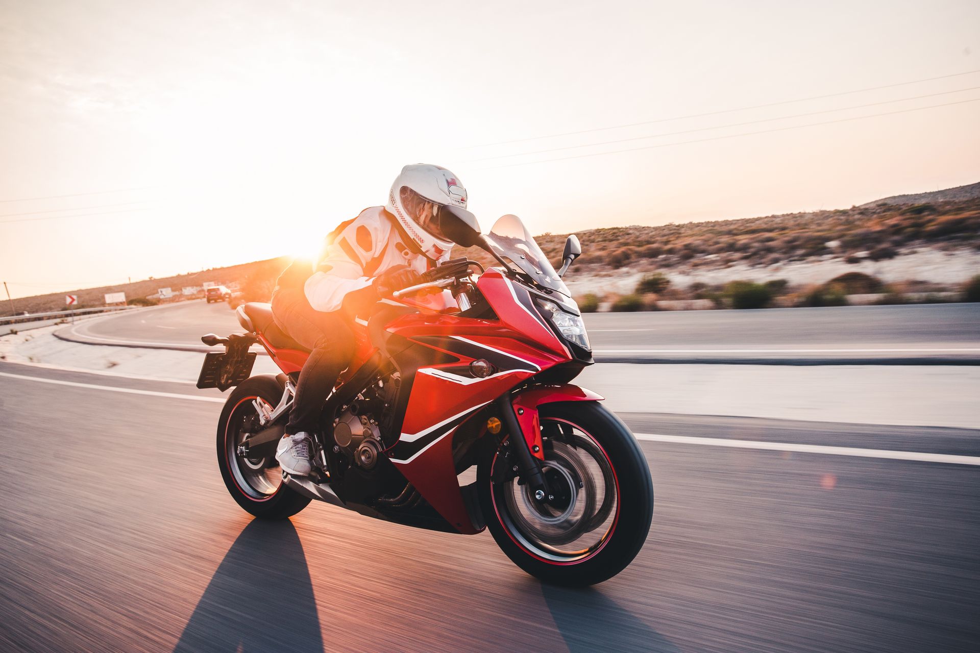 Red motorcycle speeding on a highway with a rider in full gear; sunset in the background.