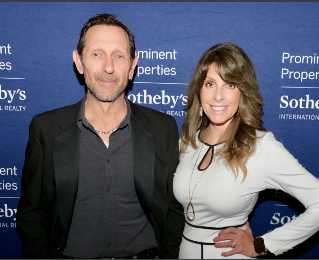 A woman is sitting at a desk with a laptop and a vase of flowers.