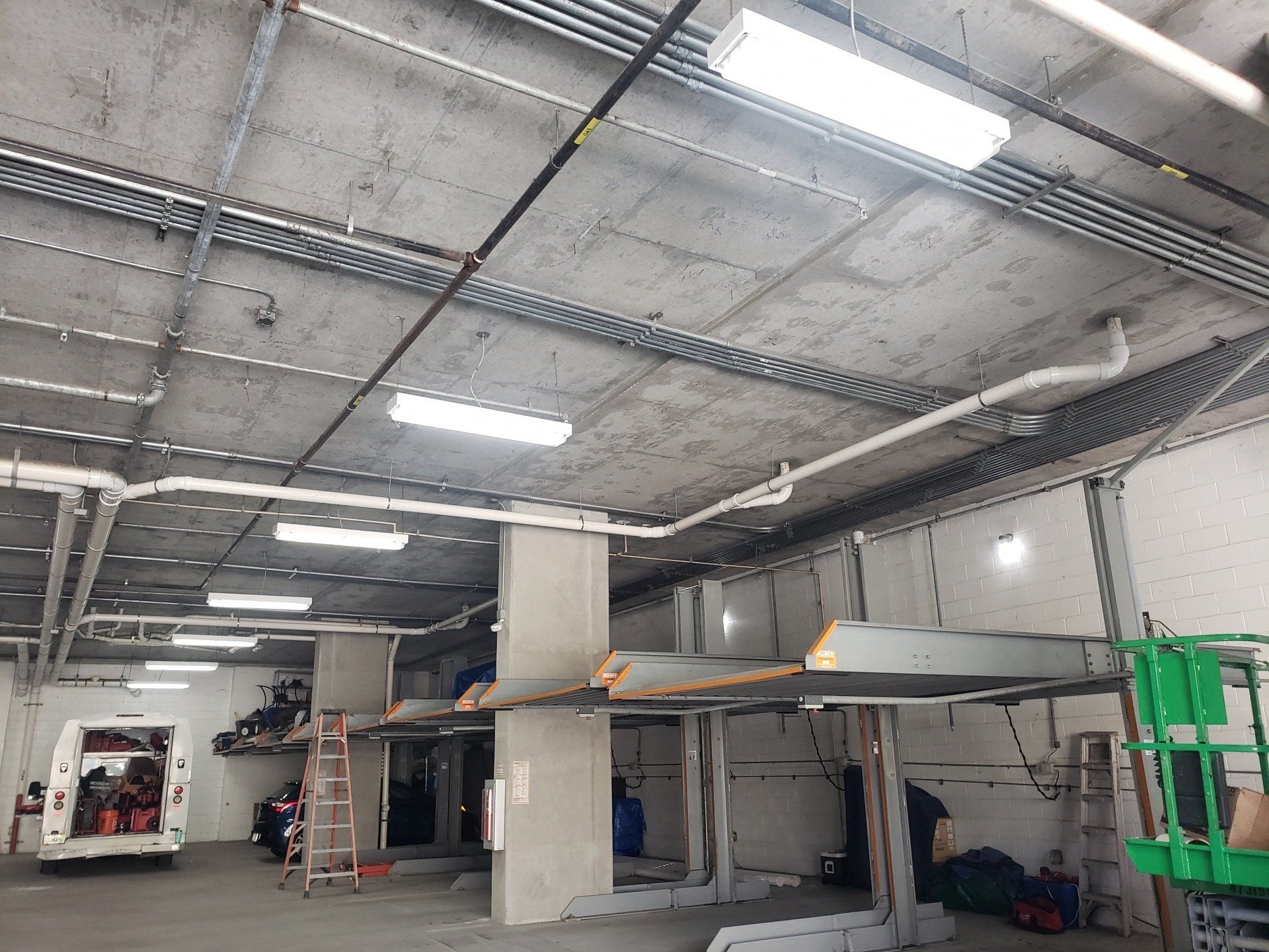 Parking garage under construction, with exposed concrete ceiling, conduits, and car lifts.