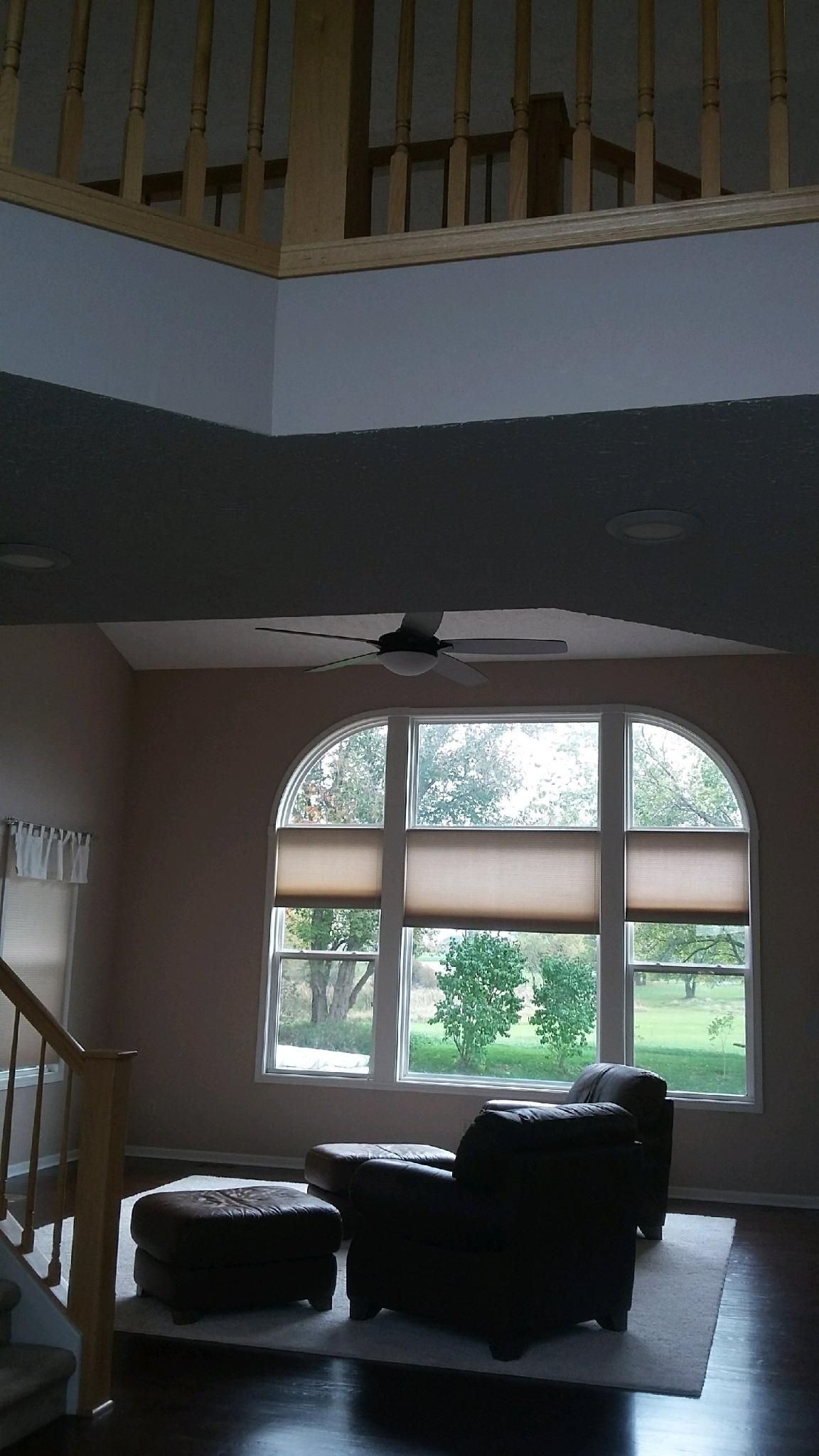 A living room with arched windows, a dark chair, and an ottoman. A staircase leads to an upper level.