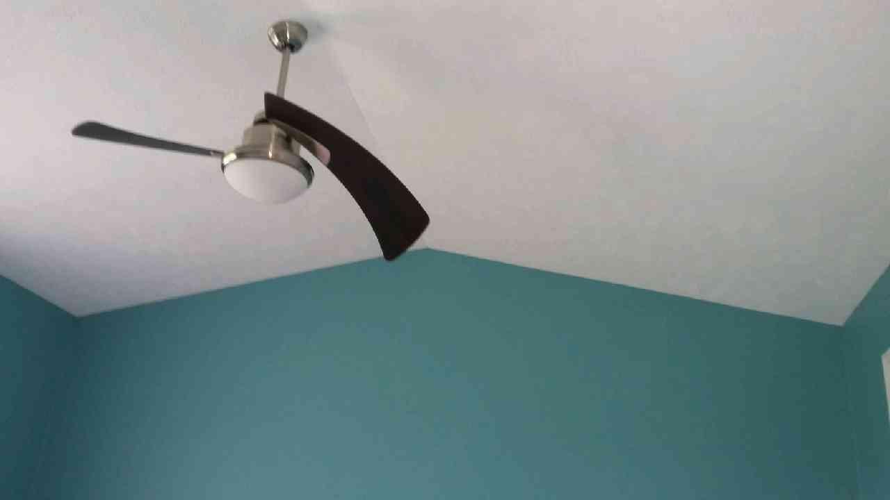 Ceiling fan with one dark brown blade, hanging in room with teal walls.