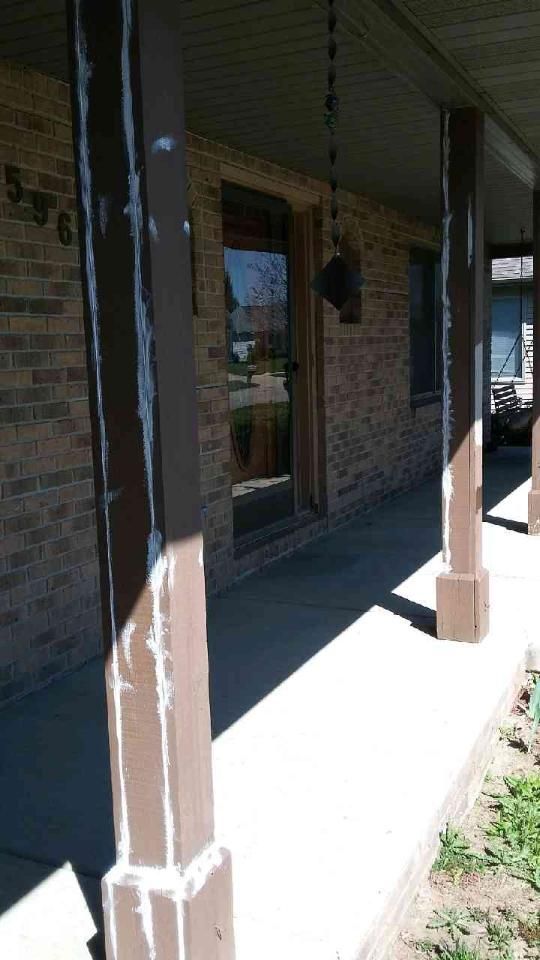 Front porch with brown columns and a brick wall.