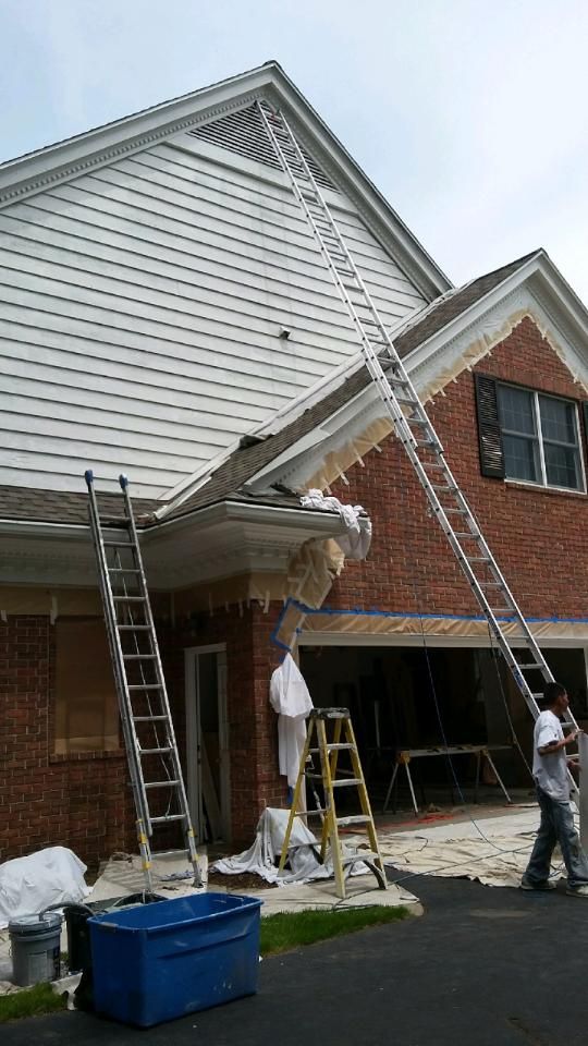 Ladders propped against a house for work. Workers near a garage, brick building, and blue sky.