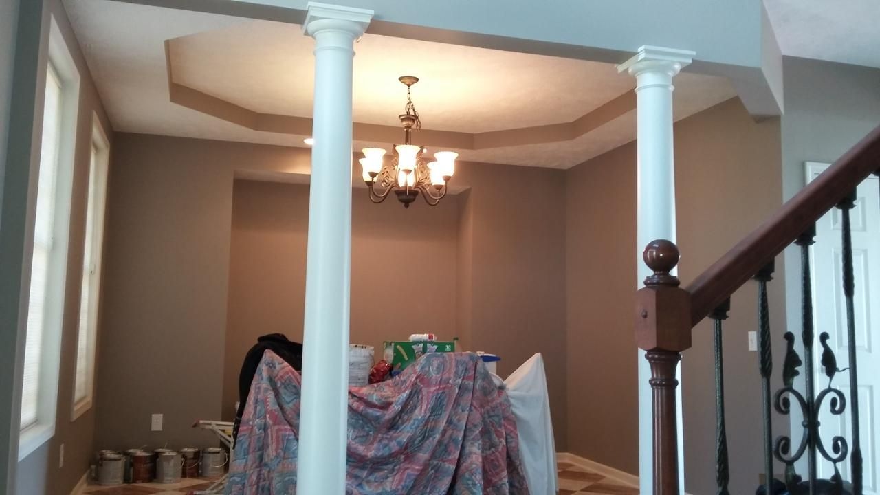 Interior room with white columns, chandelier, and brown walls; construction materials covered by a patterned cloth.