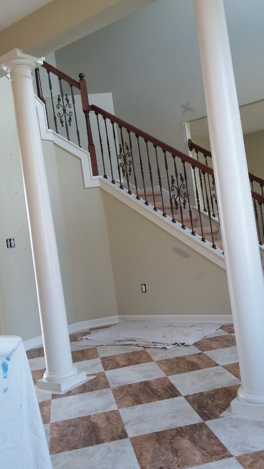 Interior with staircase, columns, and checkered floor. Cream walls, brown railing, and beige and brown flooring.