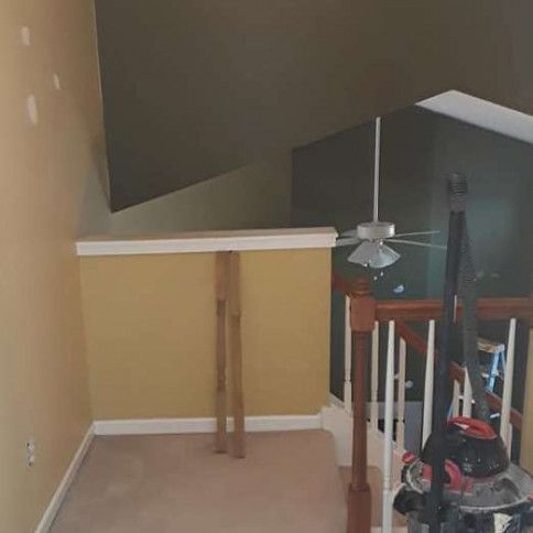 Interior view of a second floor landing and staircase. Tan and green walls, with a vacuum cleaner leaning against the railing.