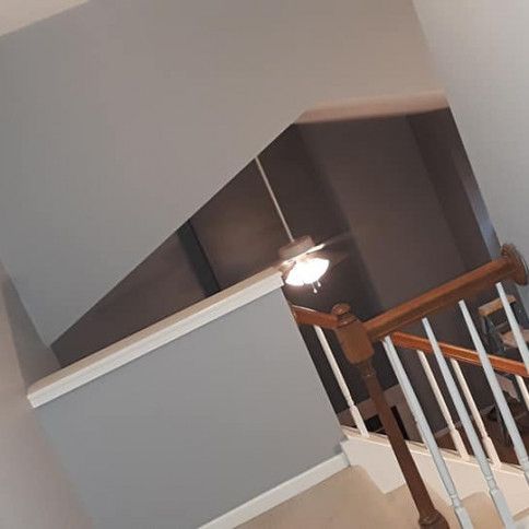 Stairwell with a gray wall, white trim, and wooden handrail. A ceiling fan is visible.
