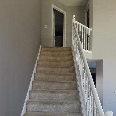 A staircase with beige carpet leads up to a doorway, white railing, and gray walls.