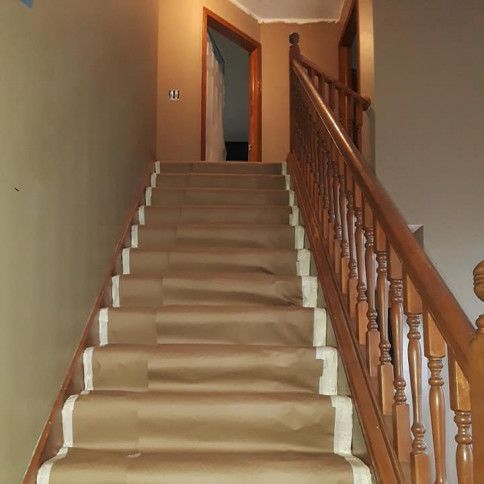 Staircase with brown paper covering steps, wooden railing, tan walls, and an open doorway at the top.
