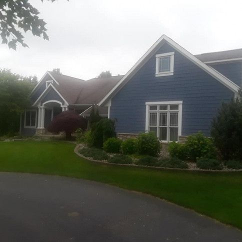 Blue house with white trim and landscaping, set on a green lawn with a driveway.