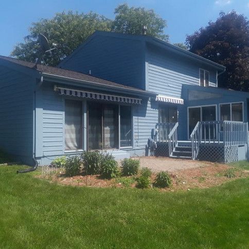 Blue house with awning, deck, and yard on a sunny day.