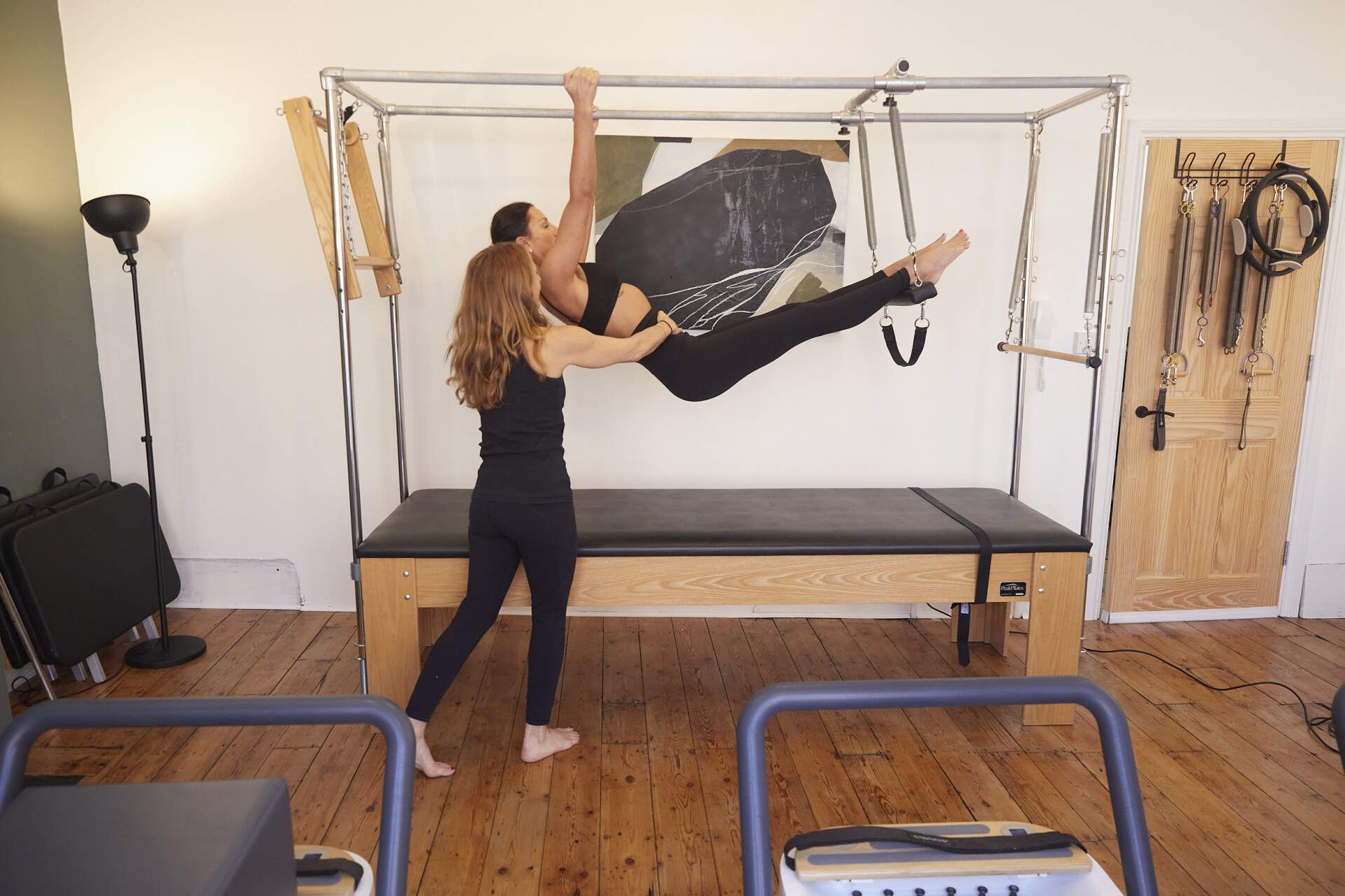 A Pilates teacher helps a student on the equipment