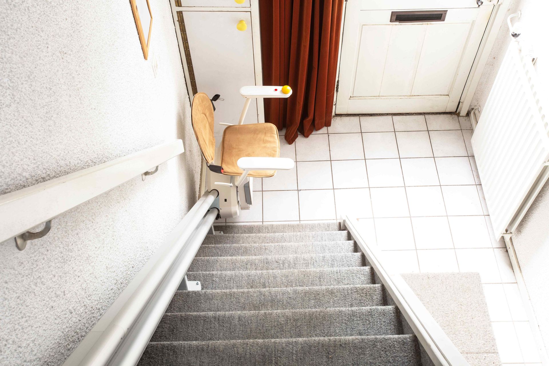 A stairlift sits at the entrance to a home, ready to usher a passenger up the stairs.