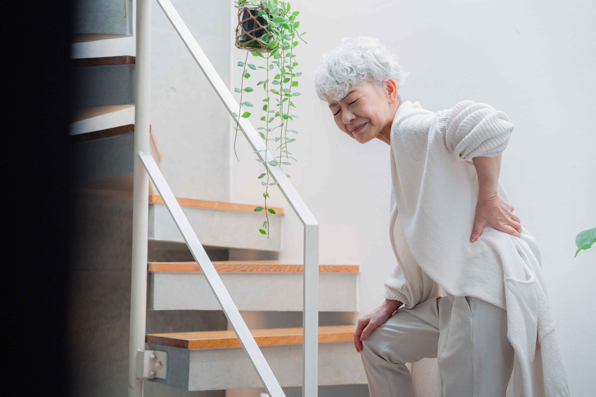 An elderly woman is struggling to walk up the stairs without pain.