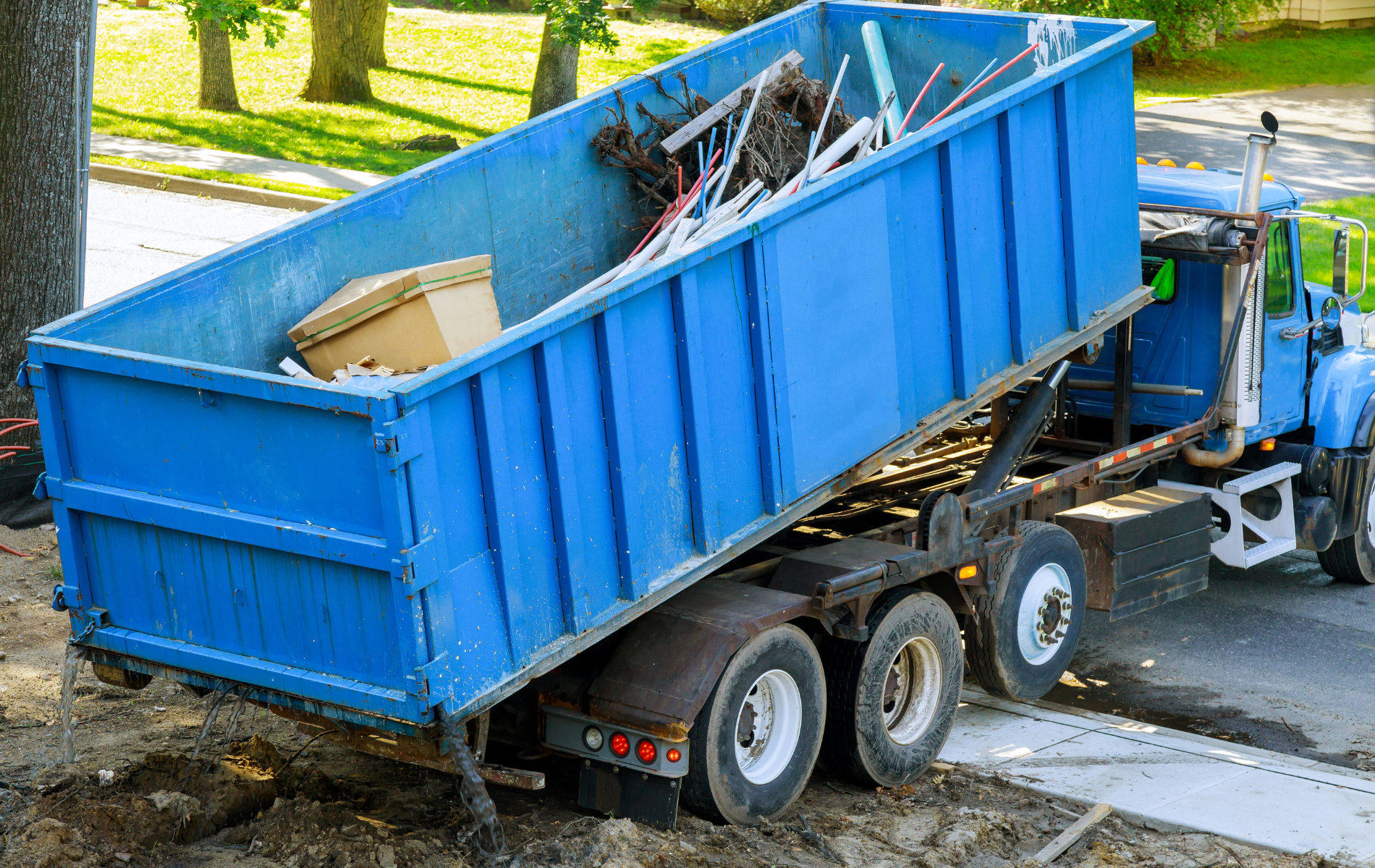 A blue dumpster truck is sitting on the side of the road.
