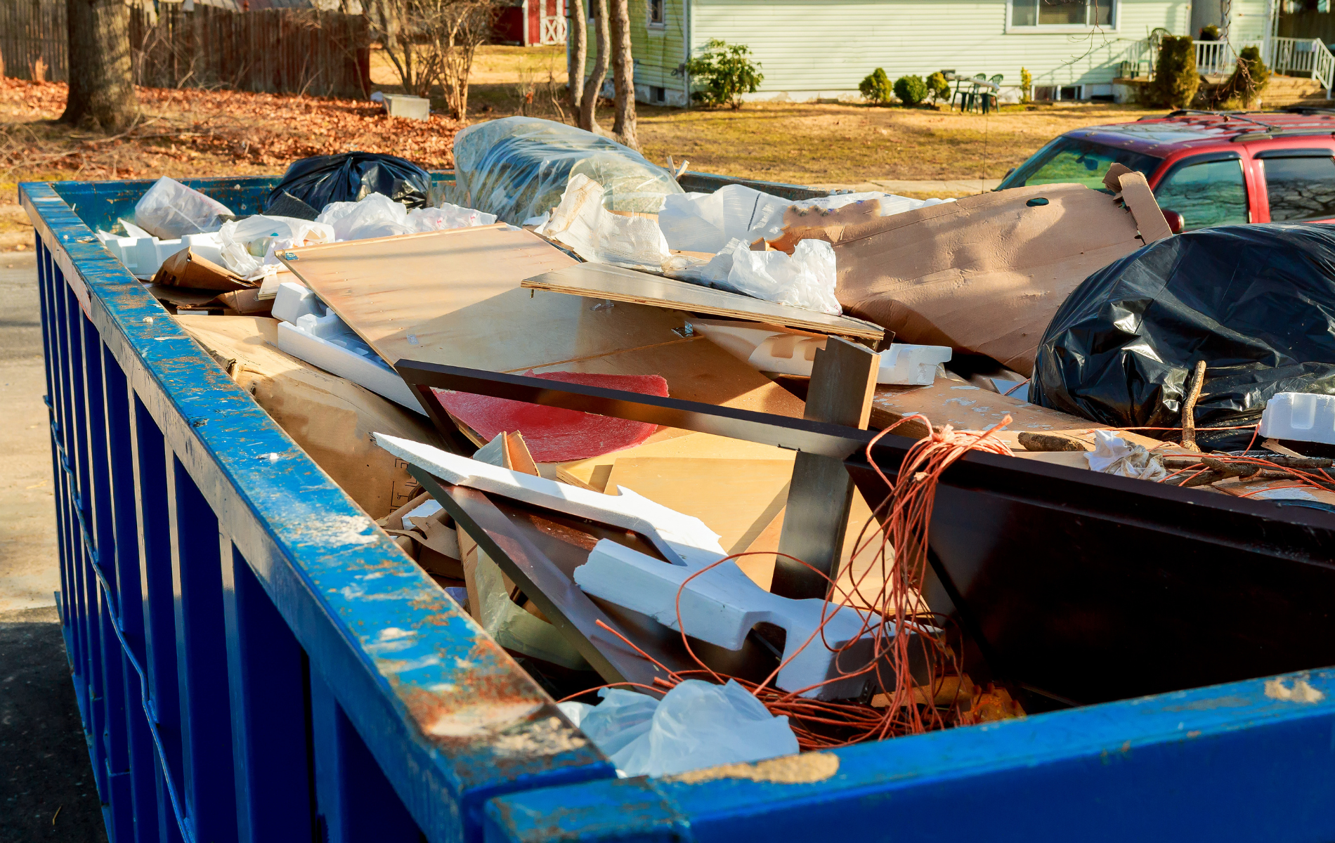 A blue dumpster filled with junk is parked in front of a house.