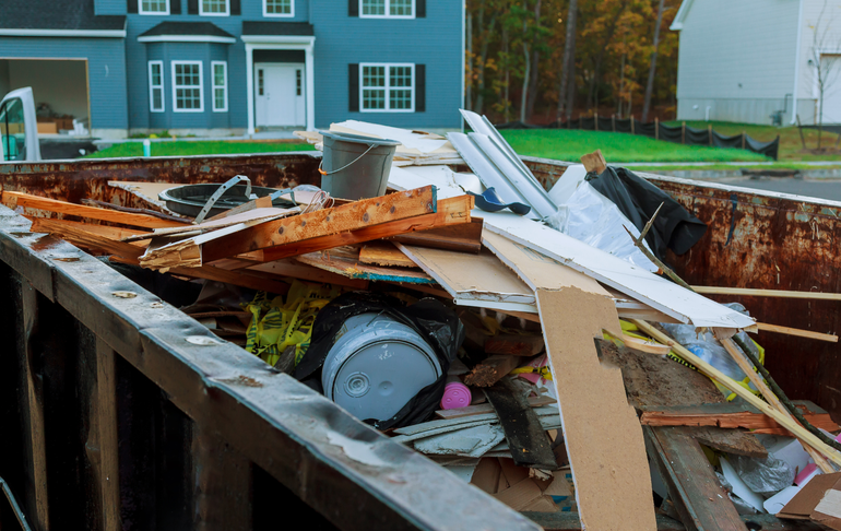 A dumpster filled with junk in front of a blue house.