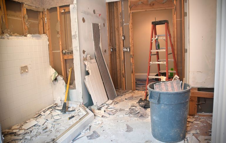 A bathroom under construction with a trash can and a ladder.