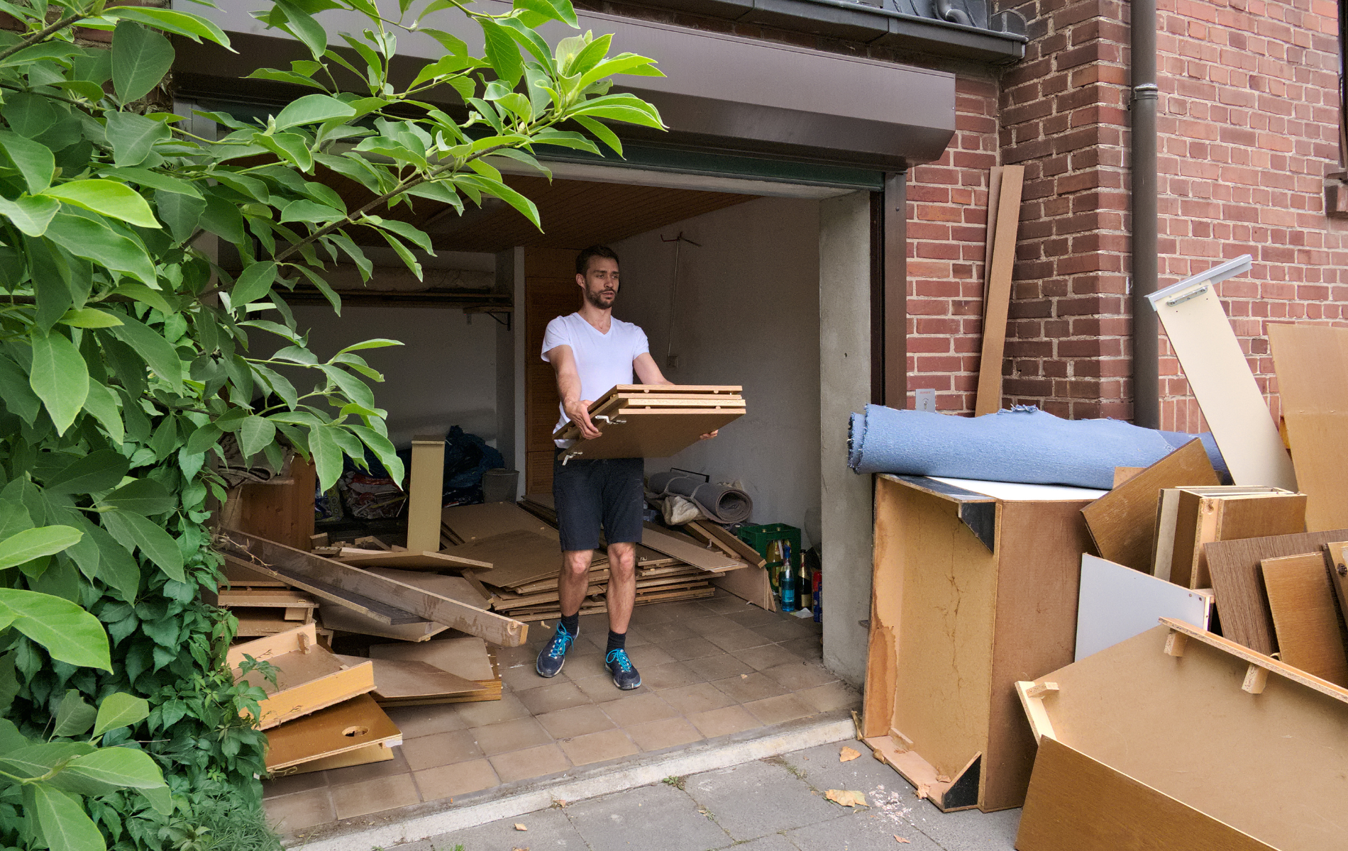 A man is carrying a piece of wood out of a garage.