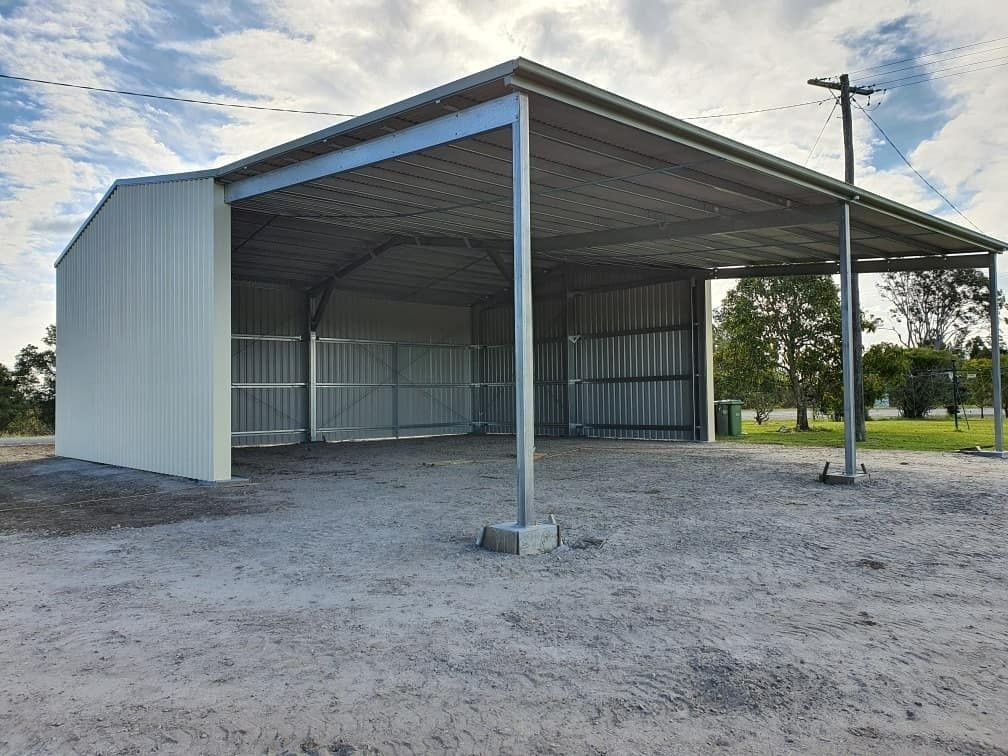 A Large, Light-colored Metal Shed With an Attached Open-sided Awning on a Gravel Surface Under a Cloudy Sky — North Coast Sheds & Garages in Coraki, NSW
