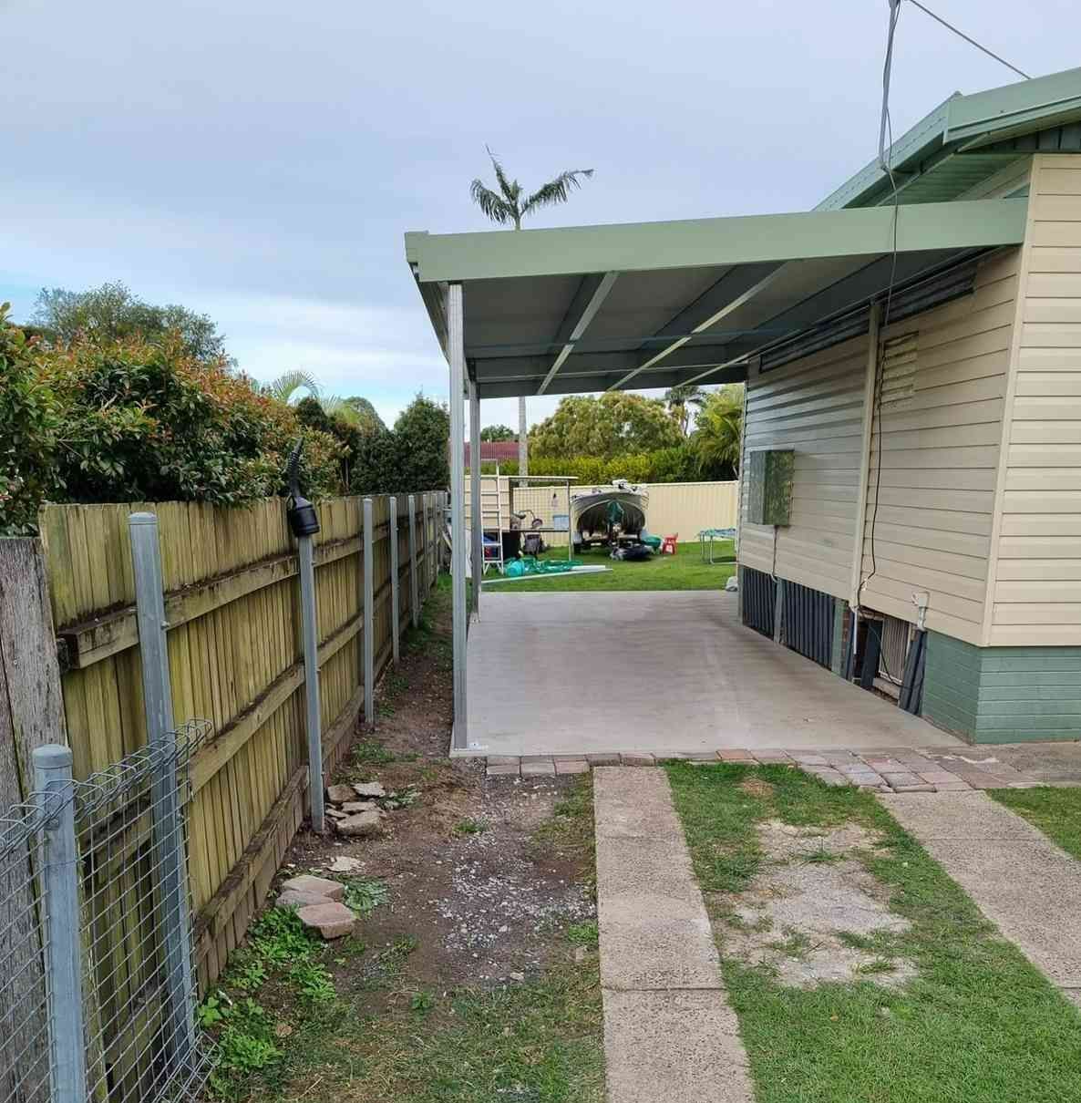 A Carport Attached to a Beige House With a Concrete Driveway. a Wooden Fence and Grass Border the Driveway — North Coast Sheds & Garages in Coraki, NSW