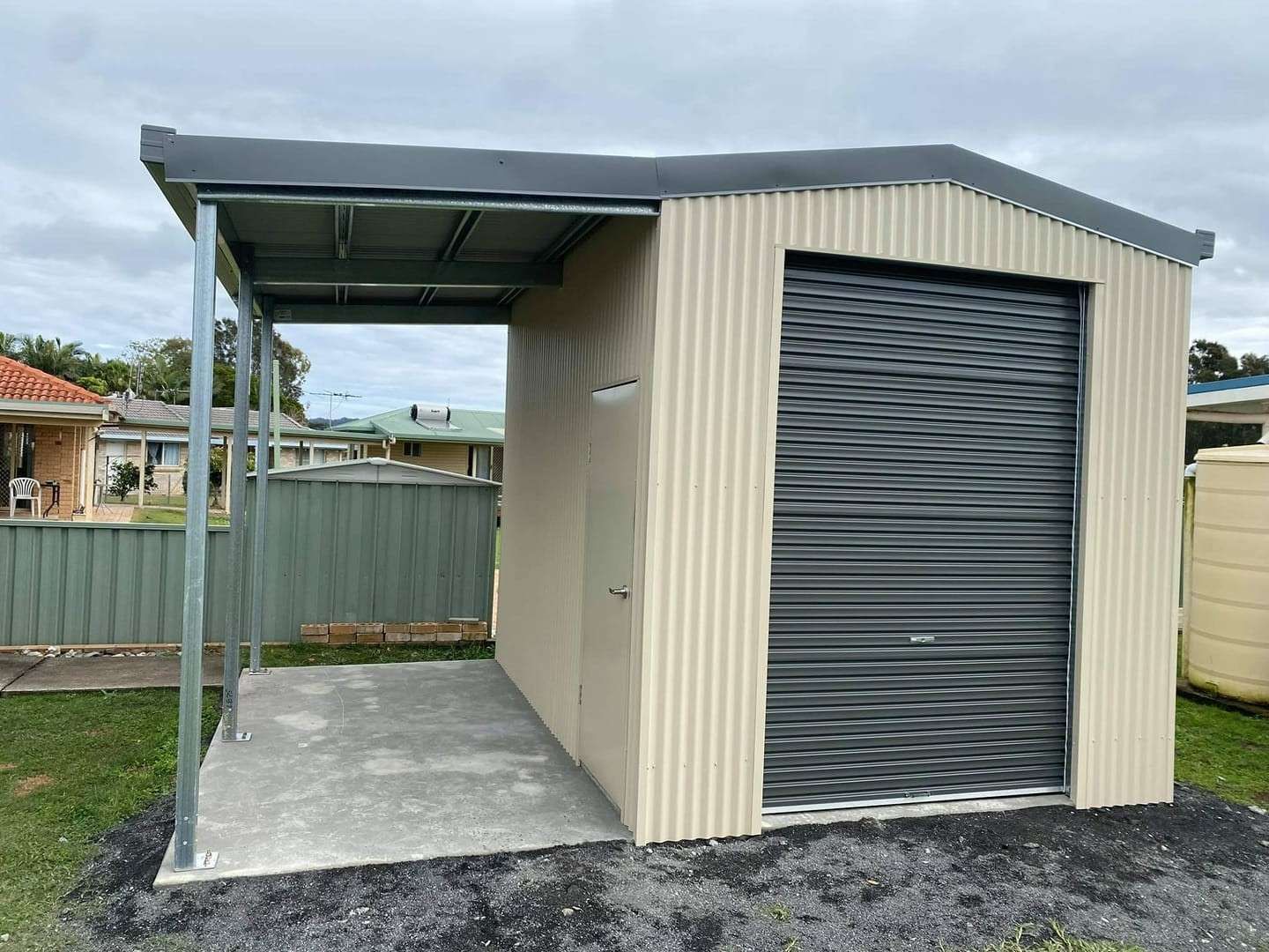 Tan Corrugated Metal Shed With a Gray Roller Door and a Covered Entryway, Set on a Concrete Pad — North Coast Sheds & Garages in Coraki, NSW