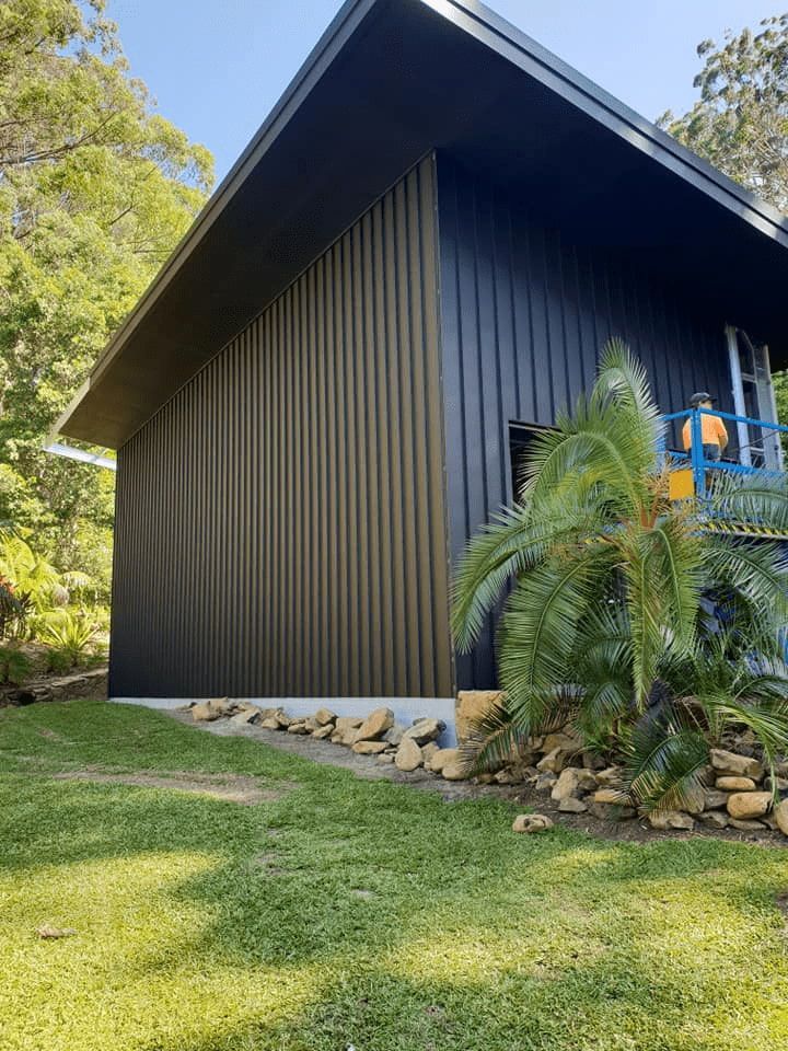 A Black-sided Building With a Sloped Roof Sits on a Concrete Base, Surrounded by Green Grass and Trees — North Coast Sheds & Garages in Coraki, NSW