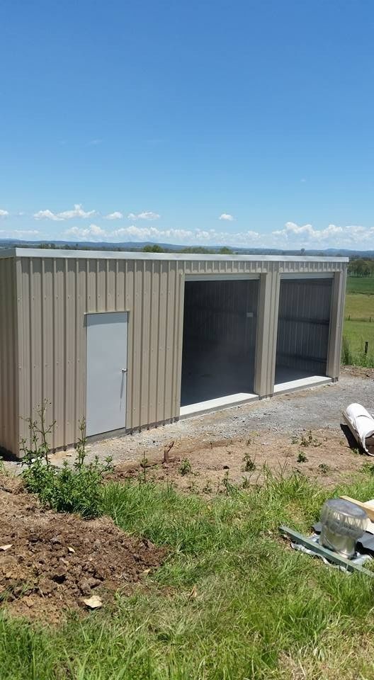 Tan Metal Shed With Two Open Garage Door Bays and a Side Door, Set on Gravel With a Blue Sky Background — North Coast Sheds & Garages in Kyogle, NSW