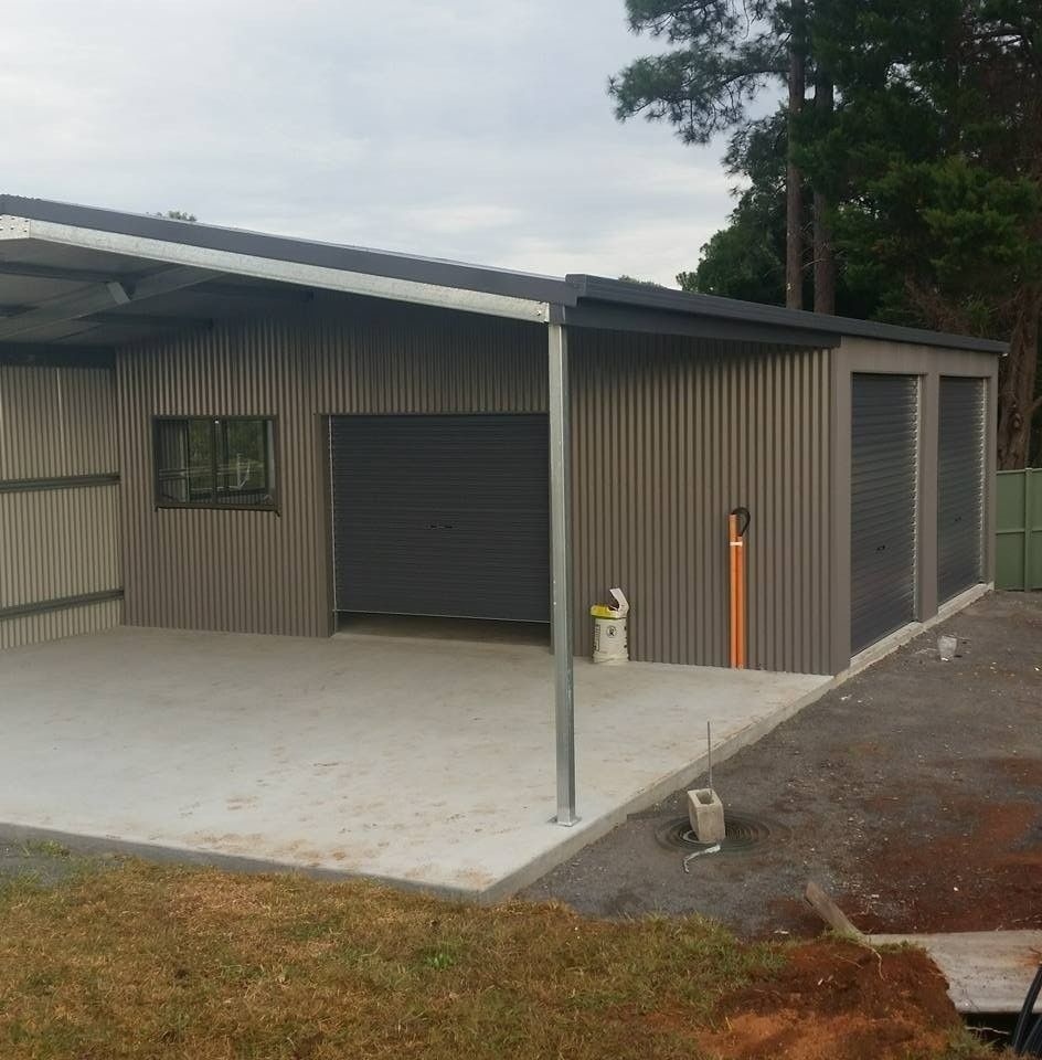 Gray Corrugated Metal Garage With a Concrete Floor and Carport Attached. in a Grassy Area, With Two Rollup Doors and a Window — North Coast Sheds & Garages in Lismore, NSW