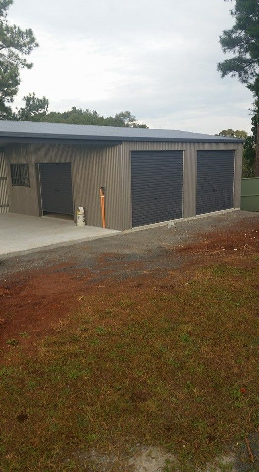 A Three-car Garage With Dark Gray Doors and a Light Gray Exterior, Sitting on a Concrete Slab With a Red Dirt Yard — North Coast Sheds & Garages in Casino, NSW