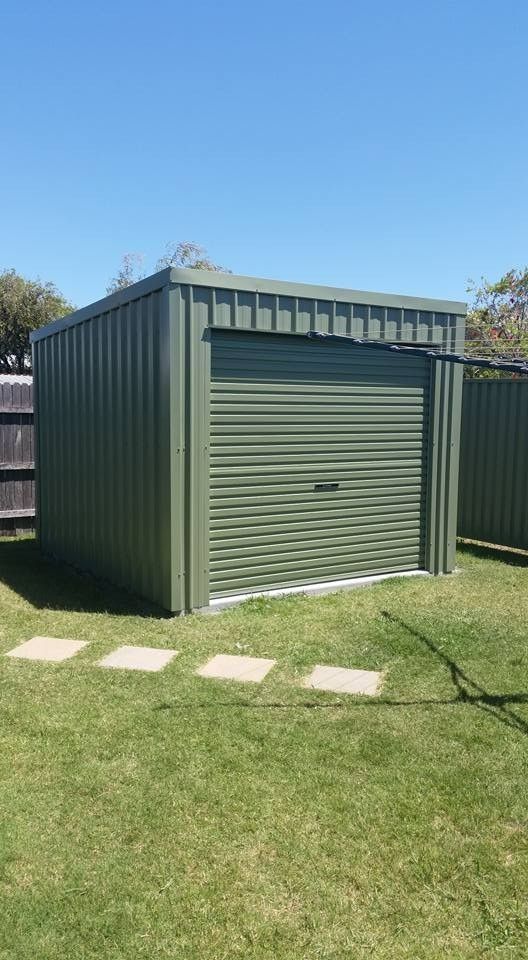Green Metal Shed With a Roll-up Door Sits on a Grassy Lawn Under a Clear Blue Sky. Stepping Stones Lead to the Shed — North Coast Sheds & Garages in Lismore, NSW