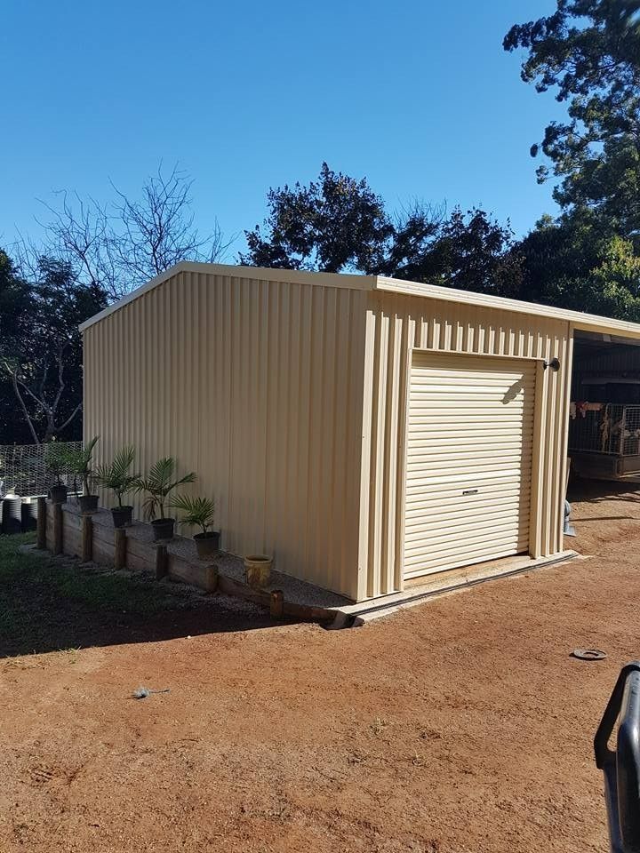 Beige Corrugated Metal Shed With a Roll-up Door, Set on a Gravel Yard Under a Blue Sky — North Coast Sheds & Garages in Bangalow, NSW