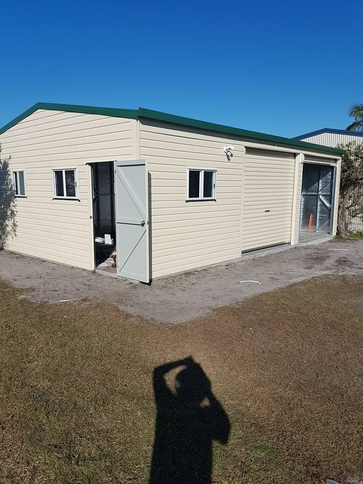 A Light Tan Shed With a Green Roof and Two Small Windows. an Open Door Shows a Glimpse of the Interior — North Coast Sheds & Garages in Byron Bay, NSW