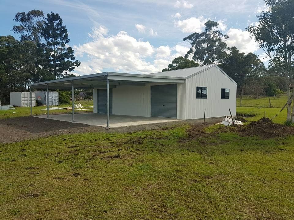 White Metal Shed With a Carport on a Grassy Field Under a Cloudy Sky. Two Garage Doors and Small Windows Are Visible — North Coast Sheds & Garages in Mullumbimby, NSW