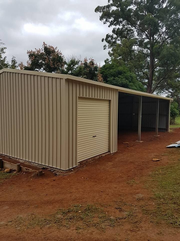Tan Metal Shed With a Roller Door and an Open-sided Awning on a Red Dirt Yard, With Trees in the Background — North Coast Sheds & Garages in The Northern Rivers, NSW