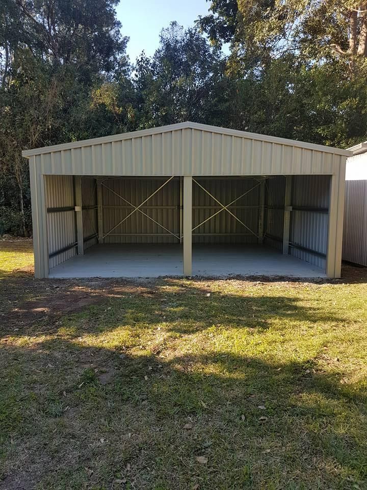 A Large, Beige Metal Carport With a Concrete Floor Sits on a Grassy Lawn, Trees in the Background — North Coast Sheds & Garages in Byron Bay, NSW
