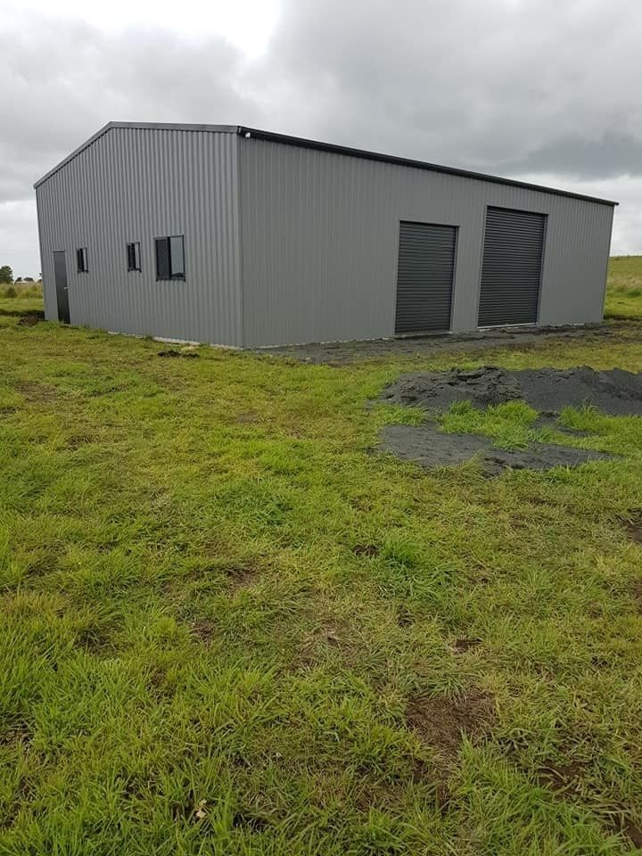 Gray Metal Shed With Two Large Roller Doors and Small Windows, Set in a Grassy Field Under a Cloudy Sky — North Coast Sheds & Garages in Coraki, NSW