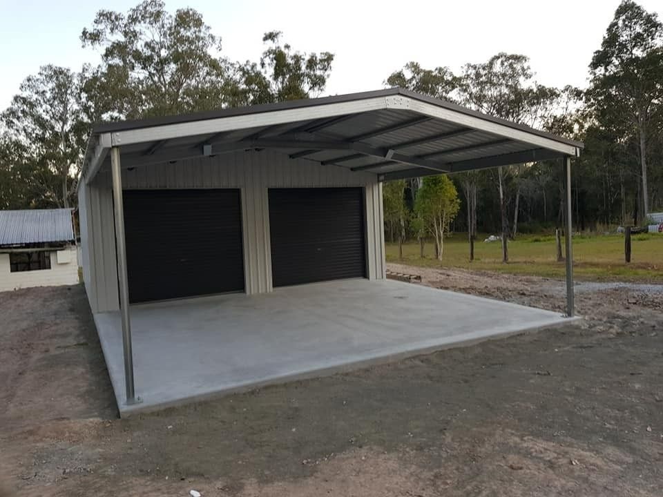 A Two-bay Carport With a Concrete Floor and Dark Garage Doors, Under a Metal Roof, Set in a Rural Landscape — North Coast Sheds & Garages in Coraki, NSW