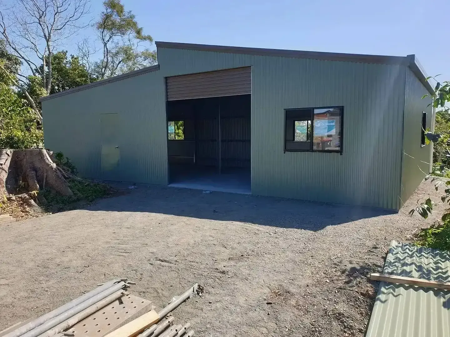 Green Corrugated Metal Shed With an Open Garage Door and a Window. Gravel Driveway in Front of the Building — North Coast Sheds & Garages in Kyogle, NSW