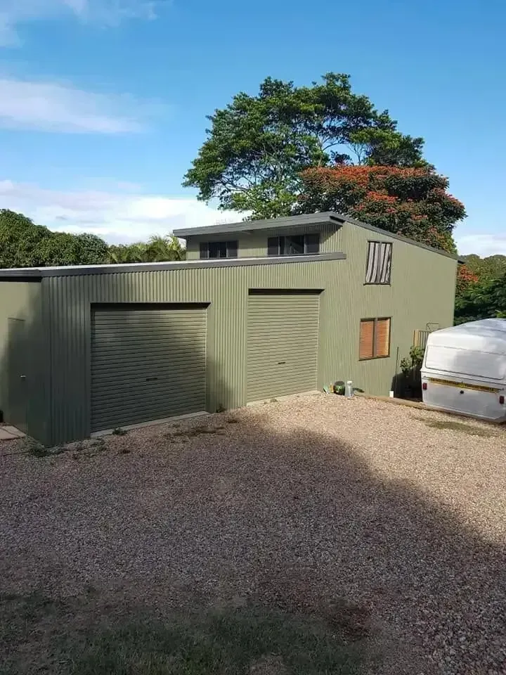 Green Metal Building With Two Garage Doors and a Second Story, Gravel Driveway, Tree in the Background — North Coast Sheds & Garages in Maclean, NSW