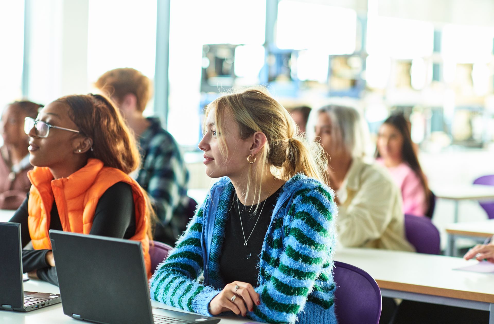 Un gruppo di persone è seduto ai banchi di un'aula con i computer portatili.