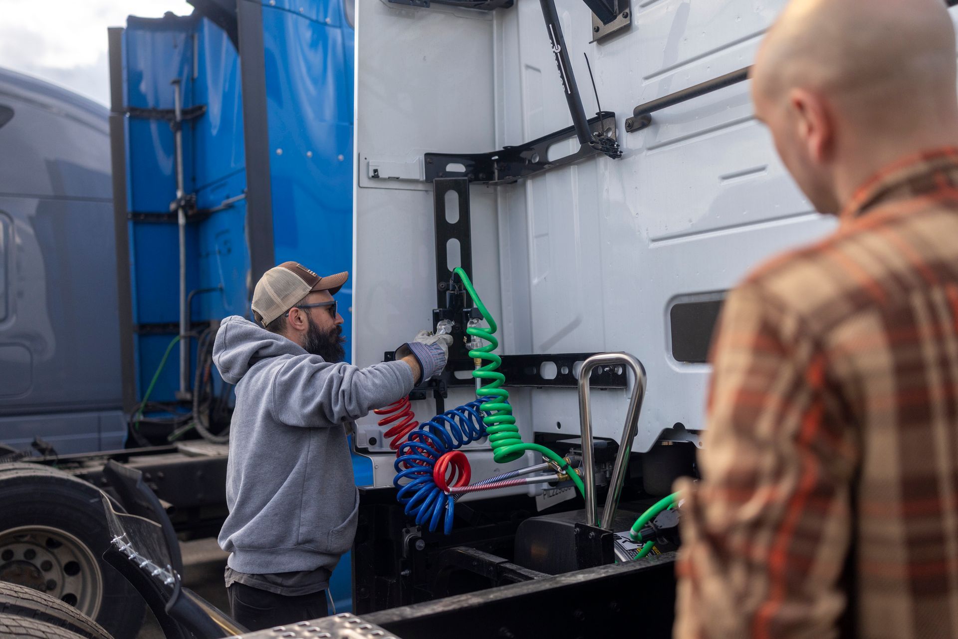 Person connecting colourful air hoses to a white semi-truck cab.
