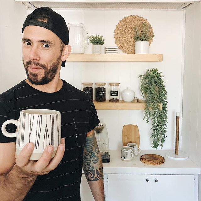 How to Build A Product that Will Make You Over $100K in Online Business. Gabriel Mayes with a cheeky smile while holding a modern mug in his minimalist kitchen to demonstrate how to build a product for a successful online business.