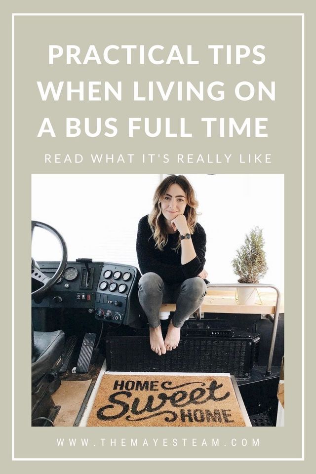 Debbie Mayes sits at the front of the skoolie as she smiles about what it's really like living on a bus full time. Image overlaid with text that reads Practical Tips When Living on a Bus Full Time Read What It's Really Like.