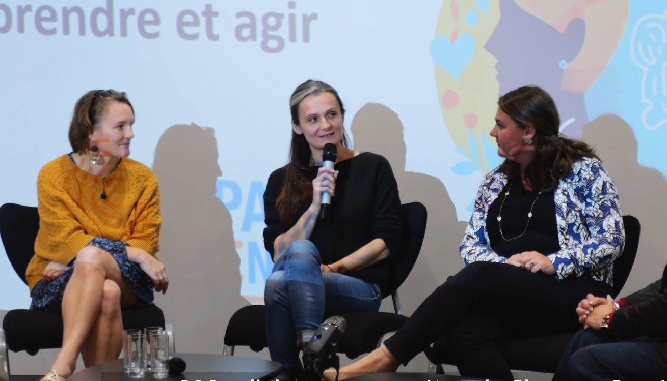 Femme et homme souriant, dos contre dos. Femme en chemise bleue, homme en pull bleu, fond brique.