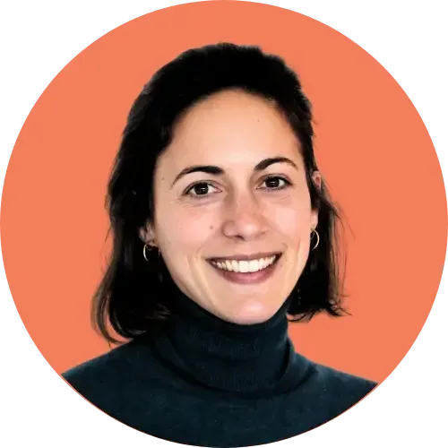 Femme aux cheveux noirs, souriant à la caméra, portant un col roulé foncé, sur fond de cercle orange.